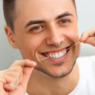 a portrait of a smiling man with a thread in his teeth being pulled from both hands